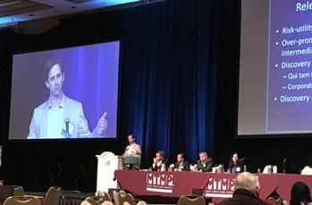 Spangenberg Attorney Speaking at a Conference at a Podium With a Panel and a Slideshow in the Background