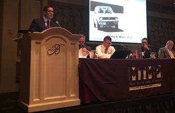 Spangenberg Attorney Speaking at a Conference at a Podium With a Panel and a Slideshow in the Background