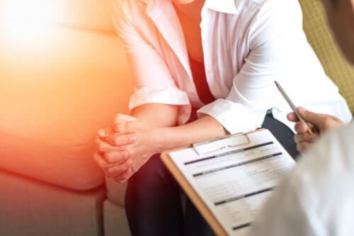 Woman Sitting on a Couch Grasping Her Hands With Man With a Clipboard and Pencil in the Foreground